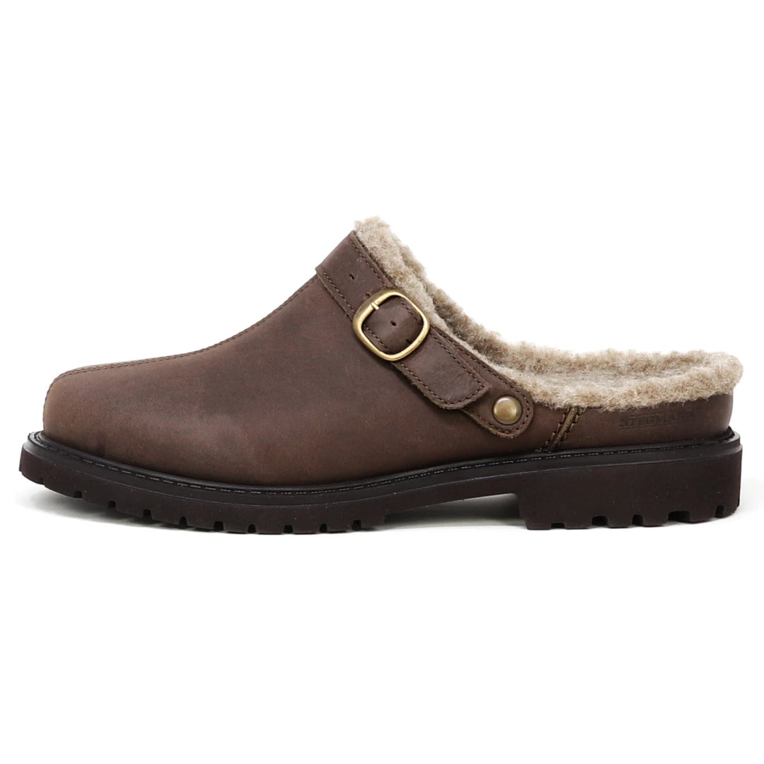 The Zermatt Wool Shearling Clog is a brown leather slip-on featuring a cozy wool shearling lining, an adjustable buckle strap, and a black rubber sole, delivering the warmth and comfort typically found in lightweight winter boots.