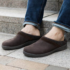 A person sits comfortably on outdoor stone steps, wearing blue jeans and Men's Halstatt Wool Lined Leather Clogs featuring a plush felt lining.