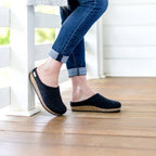 A person wearing cuffed jeans and Women's Essenz Wool Clog with a sustainable cork footbed sits on a wooden porch with legs crossed.