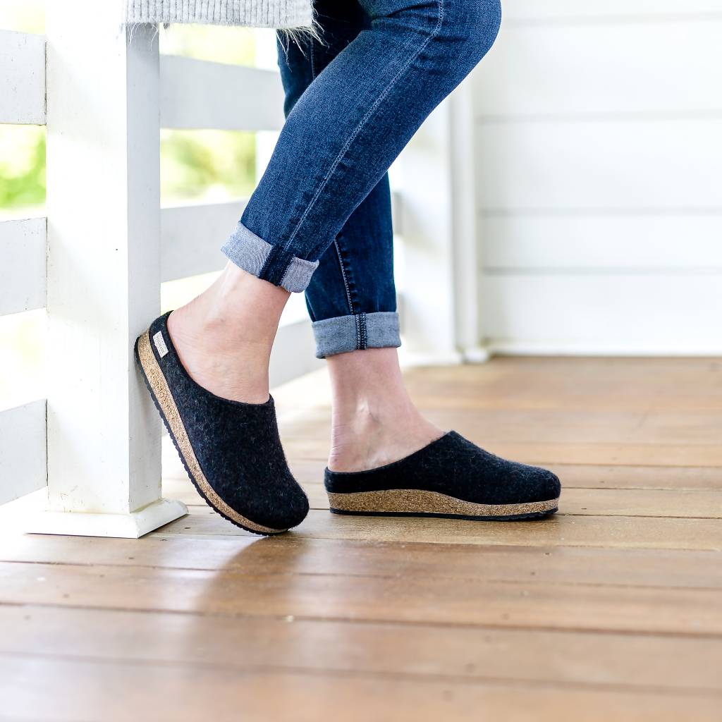 A person wearing cuffed jeans and Women's Essenz Wool Clog with a sustainable cork footbed sits on a wooden porch with legs crossed.