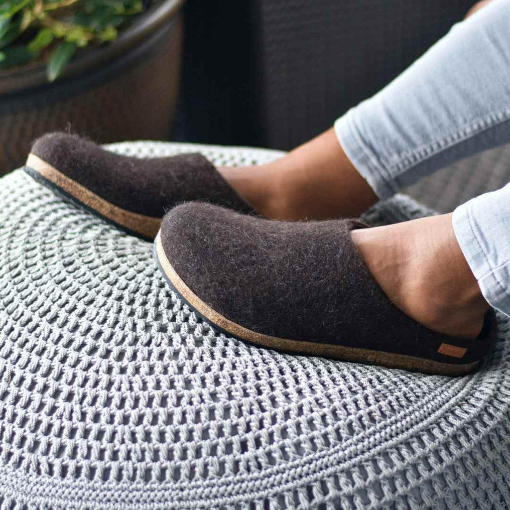 Men's Eco Clog - Jurachaf, crafted from sustainably sourced dark wool, rests comfortably on a textured gray pouf.