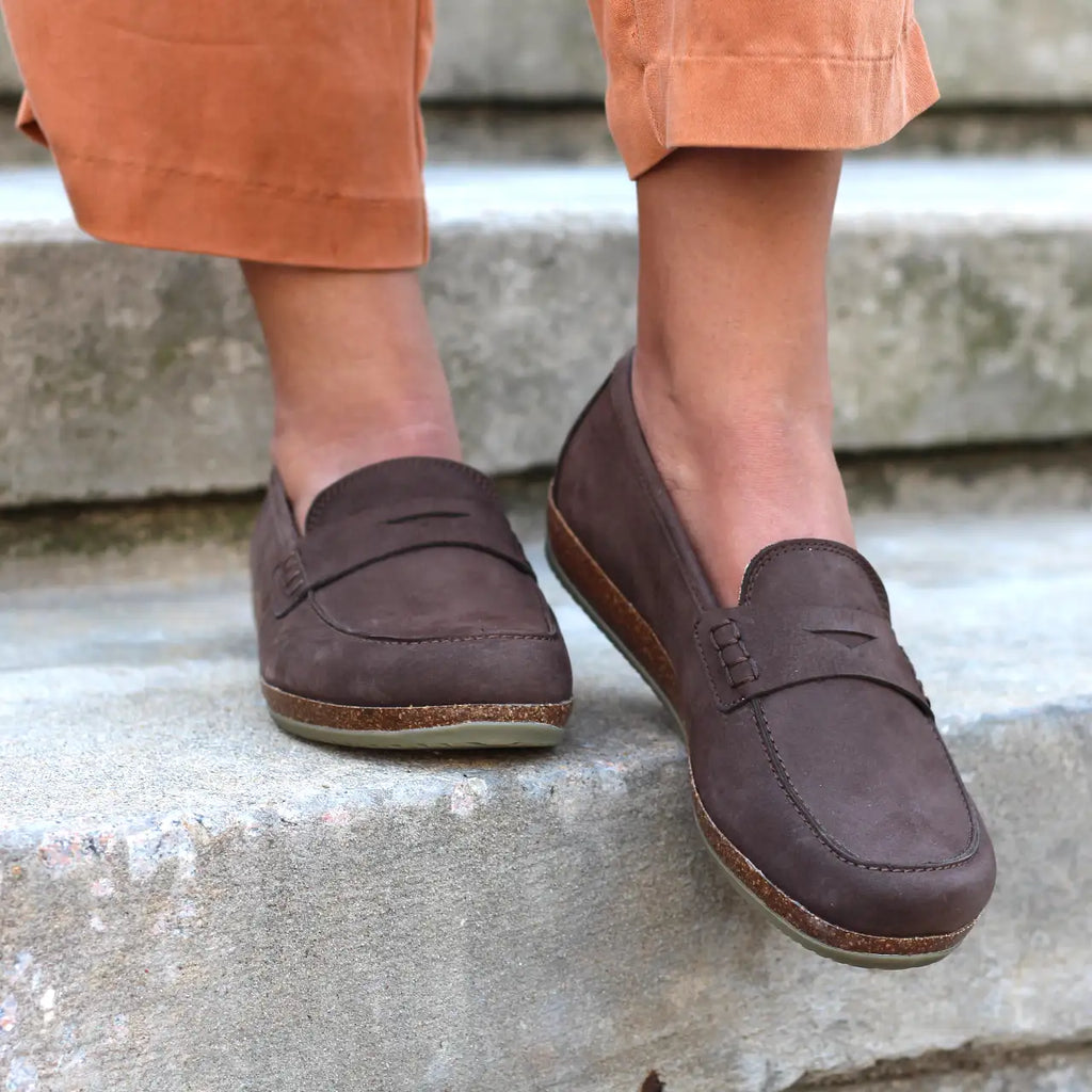 A person wearing Women's Victoria Loafer with cushioned insoles and orange pants stands on stone steps.