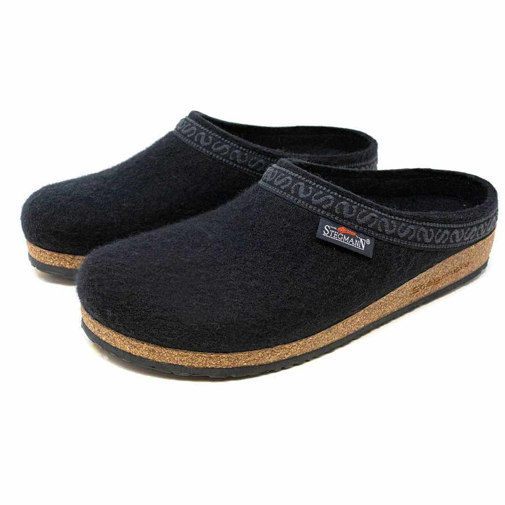 The Men's Original 108 Wool Clog is a pair of black slip-on clogs made from Merino wool, featuring cork soles and a patterned trim, designed as a stylish men's shoe with a supportive sole for comfort.