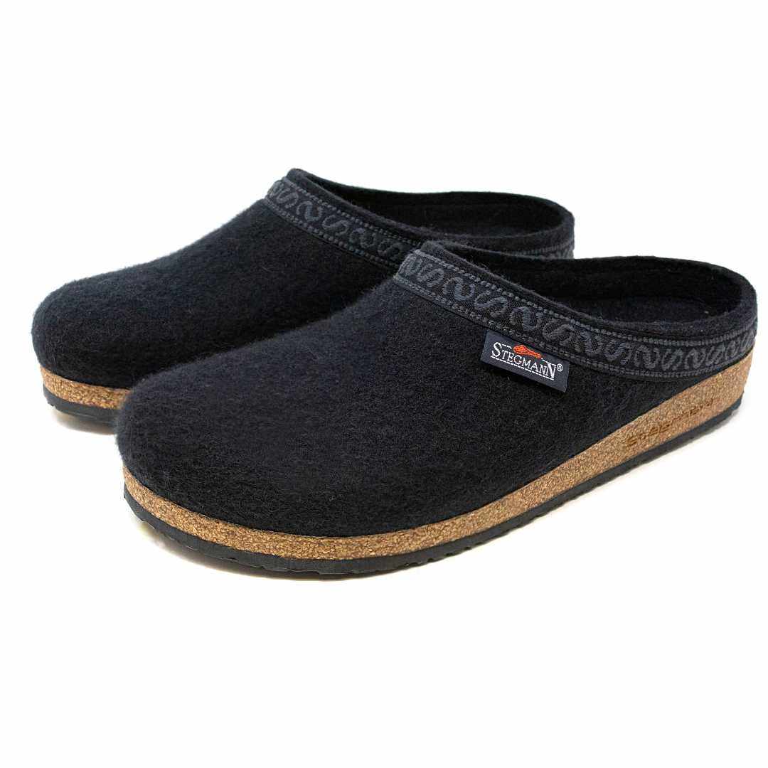 The Men's Original 108 Wool Clog is a pair of black slip-on clogs made from Merino wool, featuring cork soles and a patterned trim, designed as a stylish men's shoe with a supportive sole for comfort.