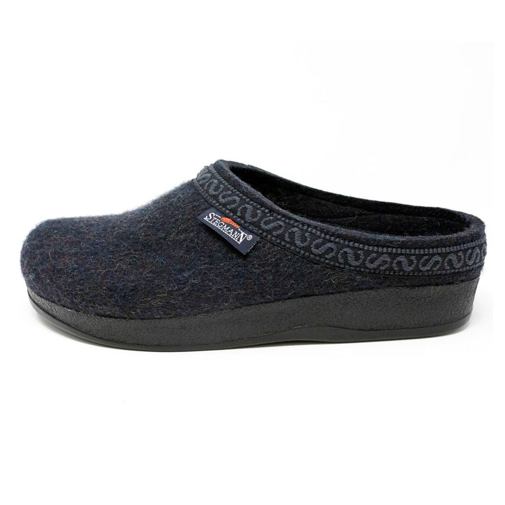 The Men's WoolFlex Wool Clog is a dark blue felt slipper crafted from Merino wool, featuring a black sole, subtle trim around the opening, and a branded side tag. The built-in arch support combines style with comfort.