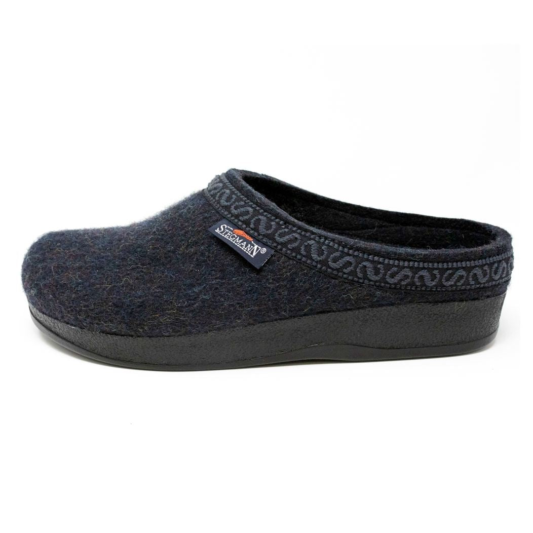 The Men's WoolFlex Wool Clog is a dark blue felt slipper crafted from Merino wool, featuring a black sole, subtle trim around the opening, and a branded side tag. The built-in arch support combines style with comfort.