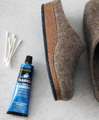 A tube of Barge Shoe Repair Cement, brown felt slippers, and several cotton swabs rest on a gray surface.