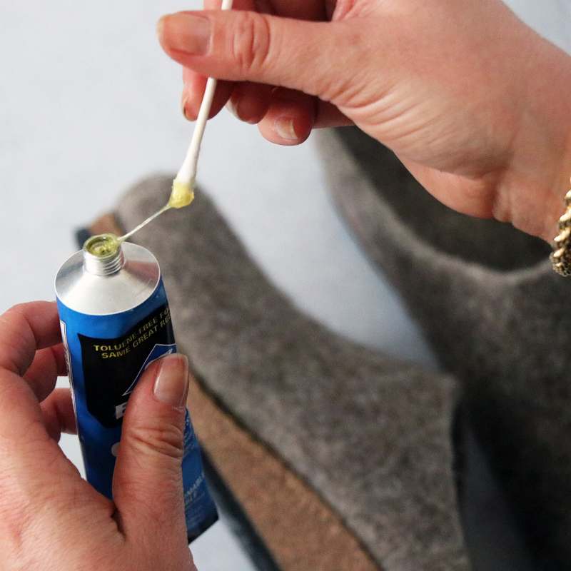 Using a cotton swab, an individual carefully applies Barge Shoe Repair Cement to a wool shoe, ensuring a precise and efficient repair.