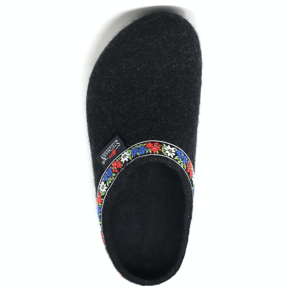 This medium "Women's Edelweiss Wool Clog" is a black slipper with floral trim at the opening and an embroidered band of red, white, and blue flowers. The elegant "Stegmann" branding on the side adds a charming touch reminiscent of traditional Edelweiss clogs.