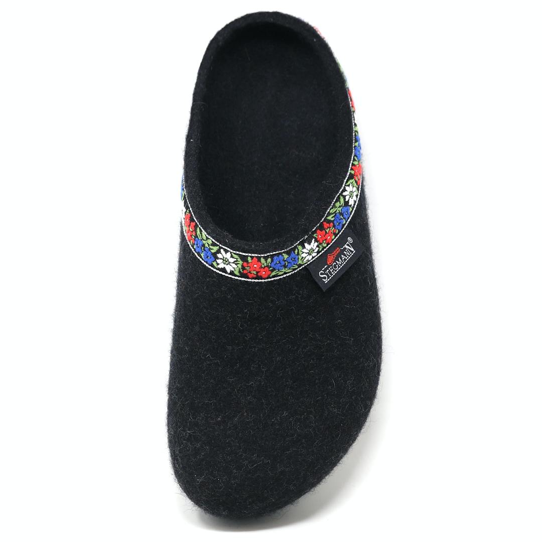 This medium "Women's Edelweiss Wool Clog" is a black slipper with floral trim at the opening and an embroidered band of red, white, and blue flowers. The elegant "Stegmann" branding on the side adds a charming touch reminiscent of traditional Edelweiss clogs.