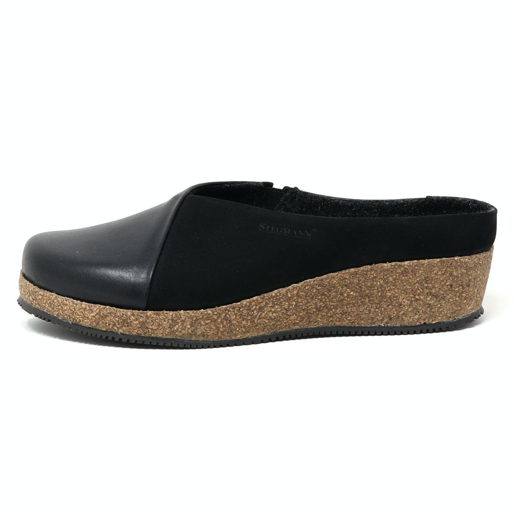 The Women's Elsa Leather & Nubuck Wedge Mule is a black slip-on featuring a cork wedge sole, smooth leather and nubuck upper, contrasting textured base, and removable wool-lined arch support insole.