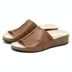 Explore the Women's Layna Leather Wedge Sandal, boasting brown leather slides with a eco-friendly cork midsole, suede footbed for added comfort, and sturdy black rubber soles.