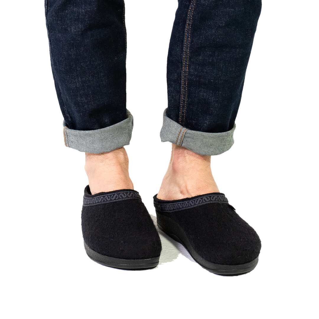 Against a white background, a person stands wearing rolled-up jeans and Men's WoolFlex Wool Clog in black, which feature arch support.