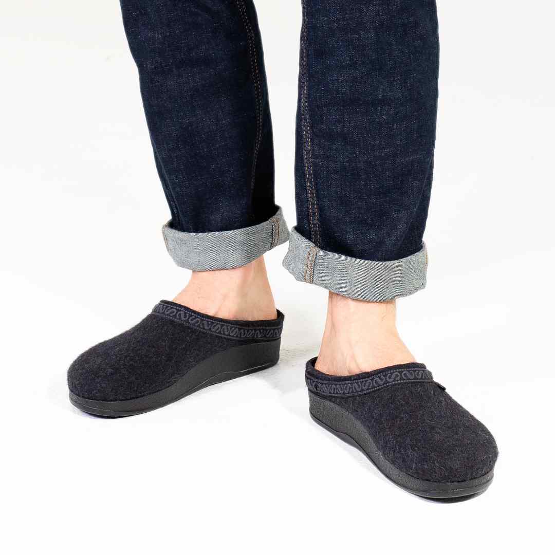 Someone stands on a white background wearing dark denim jeans with rolled cuffs and Men's WoolFlex Wool Clogs, featuring arch support.