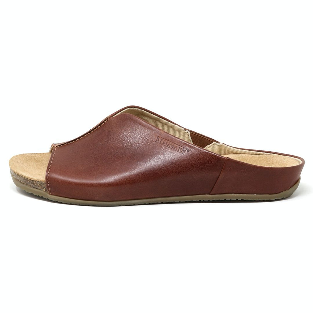 The Women's Mia Leather Slide Sandal is a brown slip-on with an open-toe design, crafted from leather. It includes a padded suede footbed and flat sole for casual wear, with an elastic gusset for added comfort.